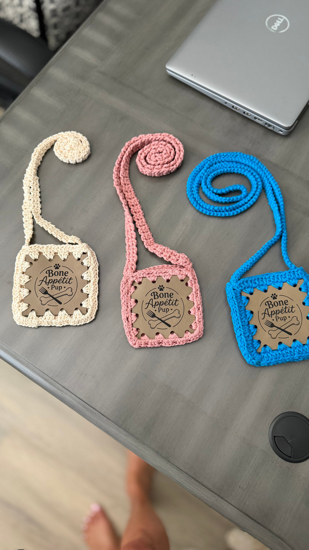 Three handmade Bone Appétit Pup crochet dog treat pouches in cream, pink and blue with long crossbody straps